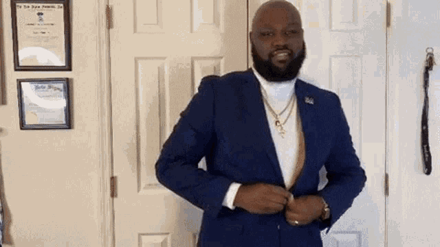 a man wearing a blue suit and a gold necklace is standing in front of a door .