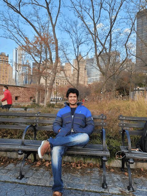 a man in a blue jacket sits on a bench in a park