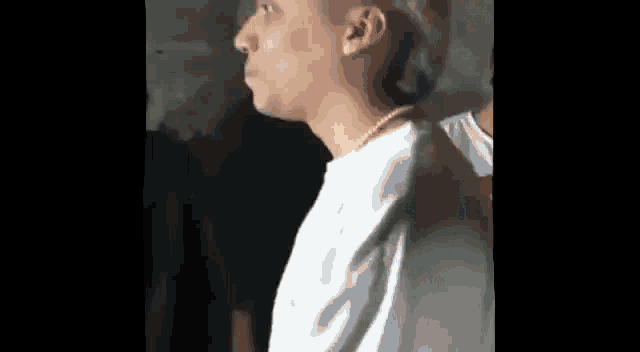 a man wearing a white shirt and a gold chain around his neck is standing in front of a wall .