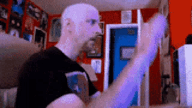 a bald man with a beard is standing in a room with a blue door and a red wall .