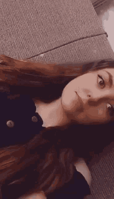 a woman with long hair is laying on a couch and making a face .