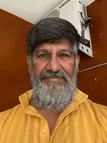 a man with a beard and a yellow shirt is smiling in front of a samsun air conditioner