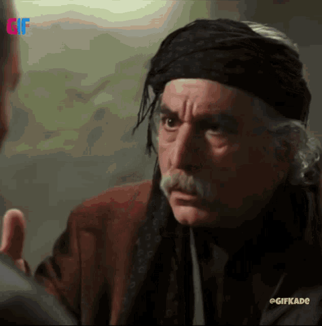 a man with a mustache is talking to another man with a gif watermark