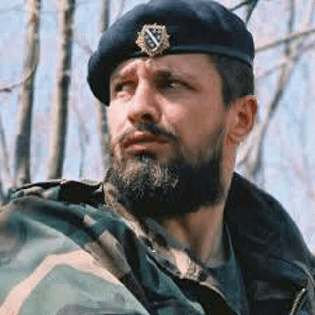 a man with a beard wearing a beret and camouflage jacket .