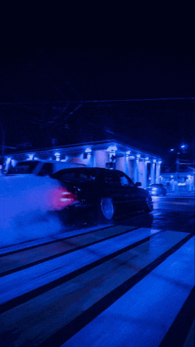 a car is driving down a street at night with smoke coming out of its tires