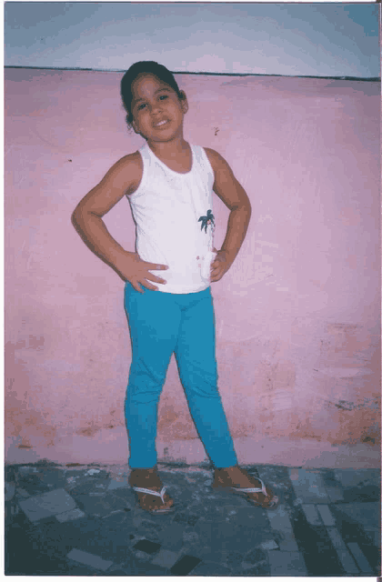 a little girl wearing blue pants and a white tank top