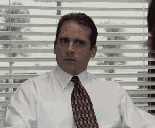 a man wearing a tie and a white shirt is sitting in front of a window