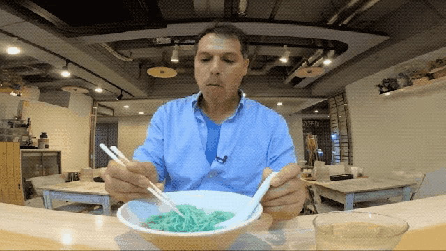 a man is eating green noodles with chopsticks