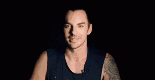 a man with a tattoo on his arm is smiling in a black tank top .