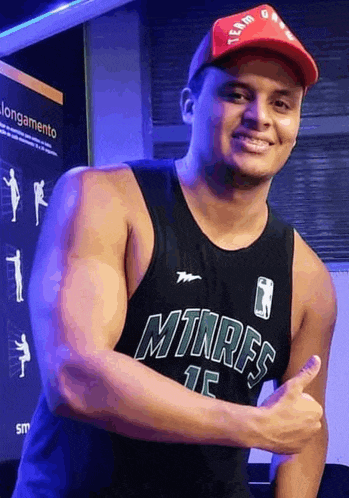 a man wearing a tank top and a hat is giving a thumbs up .