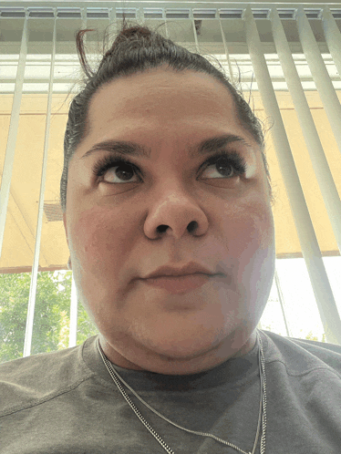 a woman wearing a gray shirt and a silver necklace looks up at the camera