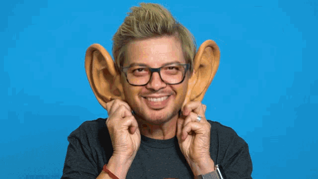 a man wearing glasses holds up his ears with the words all ears behind him