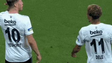 two soccer players wearing beko jerseys are standing on a field