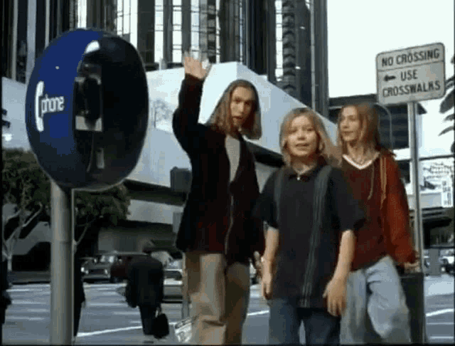 a group of people are walking down a street next to a phone booth and a no crossing use crosswalk sign .