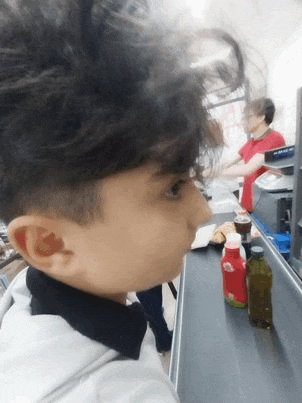 a young boy with curly hair is standing at a counter in a supermarket .