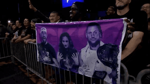 a group of people holding a purple banner with a picture of a man and woman on it