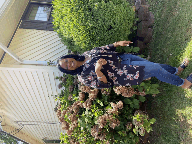 a woman is standing in front of a bush with flowers