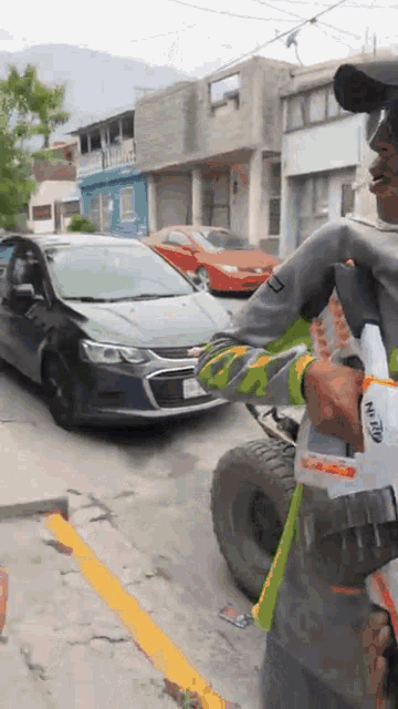 a man holding a nerf gun in front of a chevrolet