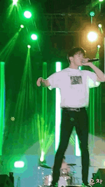 a man in a white shirt is singing into a microphone on a stage with green lights behind him