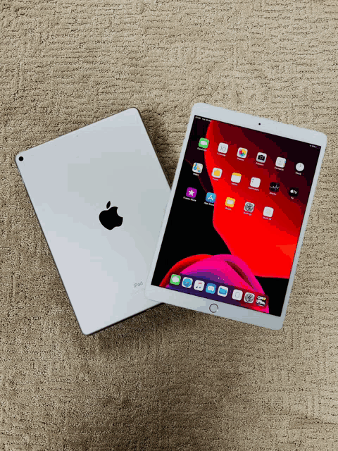 a white apple ipad sits on a carpet next to another ipad