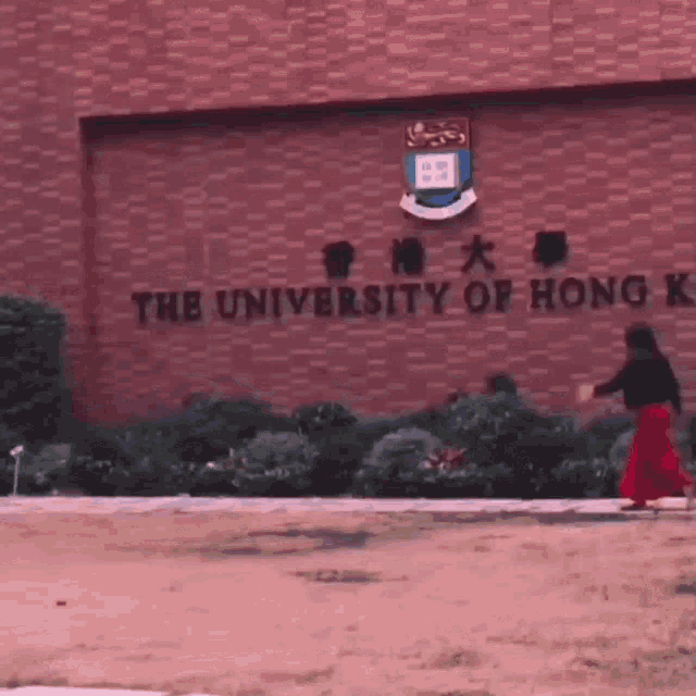 a woman in a red skirt is walking in front of a brick building that says the university of hong kong .