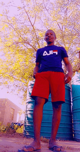 a man wearing red shorts and a blue shirt is standing in front of a water tank .