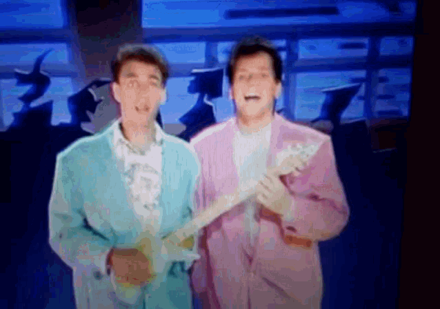 two men in pink and blue suits are holding guitars and singing