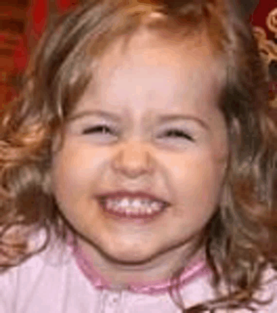 a little girl is smiling for the camera while wearing a pink shirt .