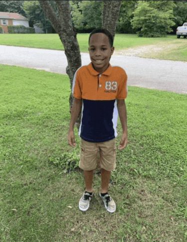 a young boy wearing a nautica shirt stands in the grass