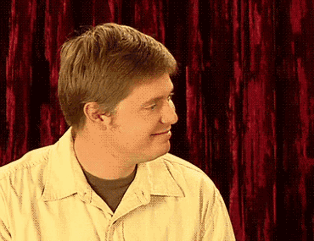 a man in a yellow shirt is smiling in front of a red backdrop