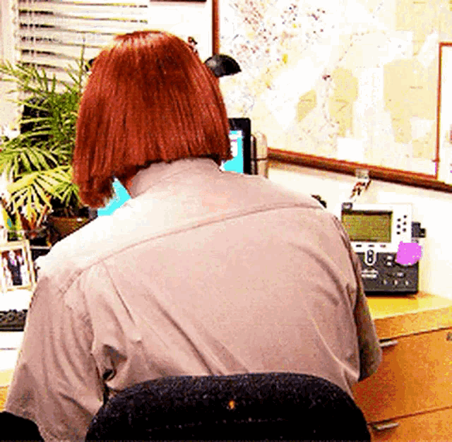 a woman with red hair is sitting at a desk with a phone and a map on the wall behind her