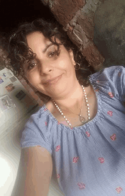 a woman wearing a striped shirt and pearls smiles for a selfie