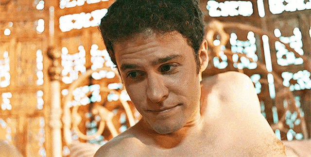 a shirtless man is looking at the camera with a blurry background