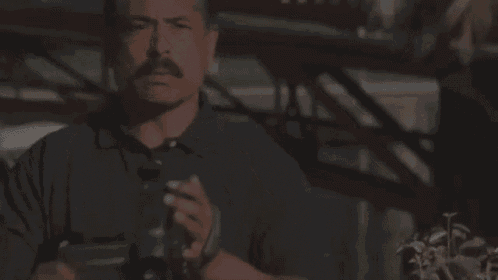 a man with a mustache is holding a camera in his right hand .