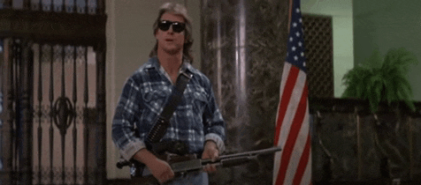 a man in a plaid shirt is holding a shotgun in front of an american flag .