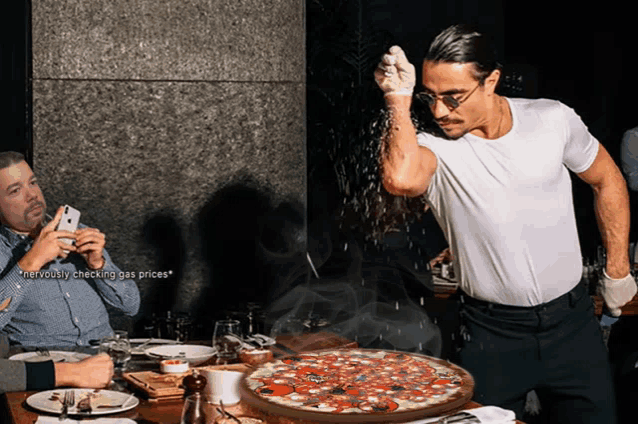 a man in a white shirt is sprinkling salt on a pizza in front of a group of people