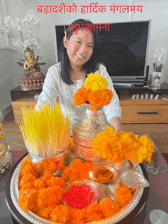 a woman stands in front of a tray of flowers with a greeting in a foreign language above her