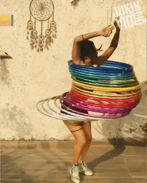 a woman is spinning a bunch of colorful hula hoops in front of a wall with a dream catcher on it