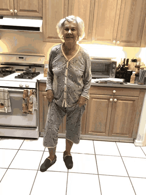 an elderly woman in pajamas stands in a kitchen