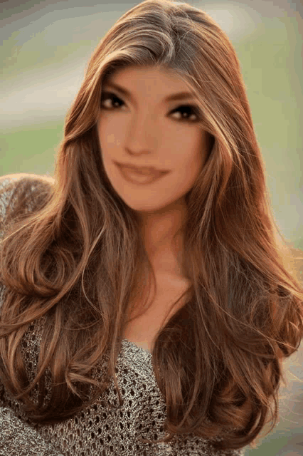 a woman with long brown hair is wearing a sweater and smiling