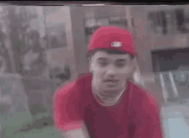 a young man wearing a red hat and a red shirt is standing in front of a building .