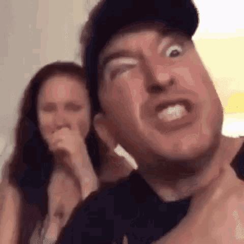 a man is making a funny face while a woman laughs in the background .