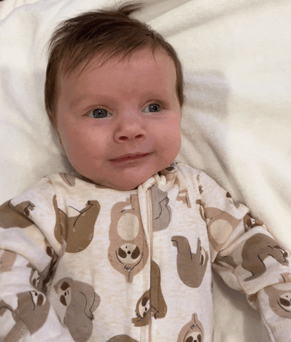 a baby wearing a sloth onesie is laying on a bed