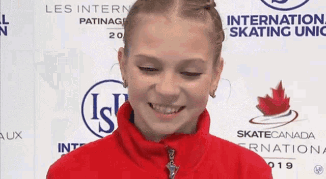 a young girl in a red jacket is smiling in front of a sign that says international skating union .