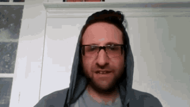 a man with a beard and glasses is wearing a hooded jacket and glasses .