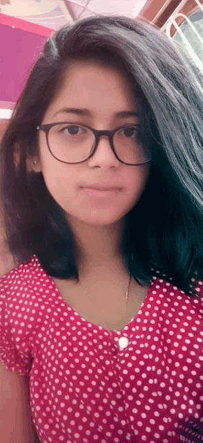 a girl wearing glasses and a polka dot shirt looks at the camera