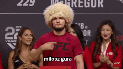 a man wearing a wig and a ufc shirt stands in front of a group of women