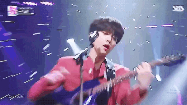a man in a red jacket is playing a guitar on stage