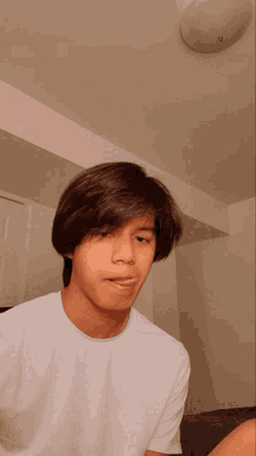 a young man wearing a white t-shirt is making a funny face