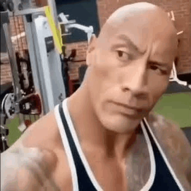 a bald man in a tank top is standing in a gym .